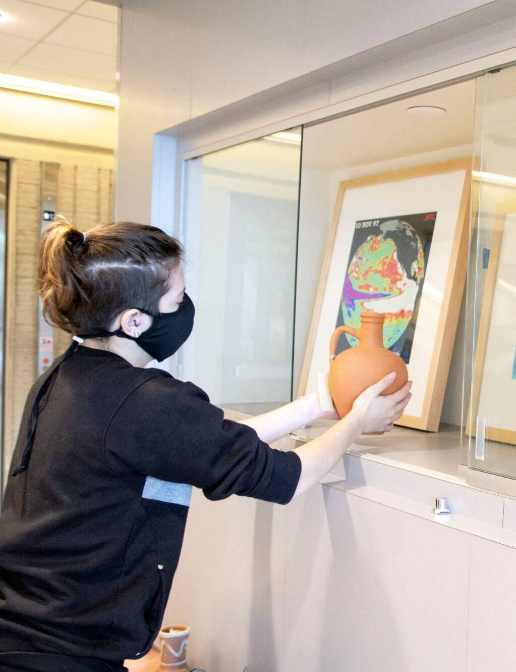 GVSU Art Museum Student hands a ceramic vase, assisting with an exhibition.